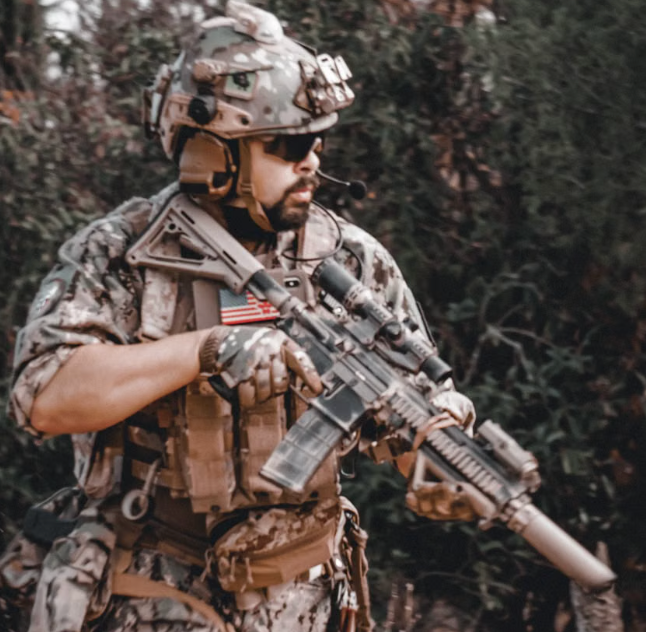 Tactical operator in camouflage gear carrying a rifle during a military field training exercise